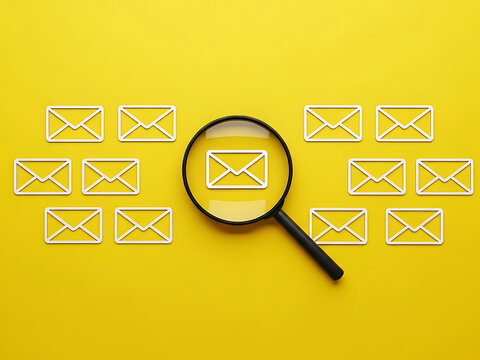 Magnifying glass examining multiple email icons on yellow background