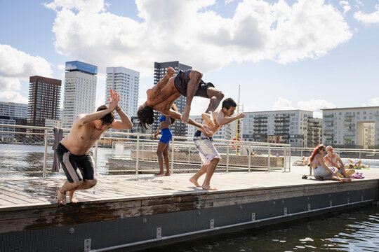 Multiracial male friends jumping together in water under cloudy sky