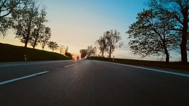POV car driving on asphalt highway with oncoming vehicles and headlights at sunset. Evening traffic passing by as point of view ride continues along smooth road. Cars approaching on opposite lane