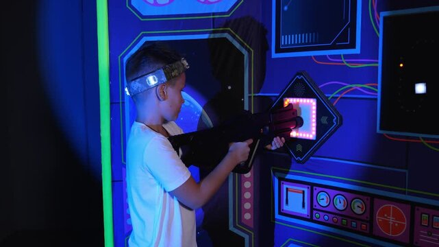 A boy in a laser tag game runs up to recharge and charges his laser weapon. An active laser tag game for teenagers. Colorful neon game arena.