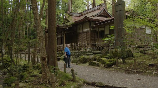Caucasian male tourist stops at stone stele by mossy temple in forest
