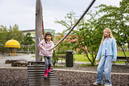 Girl holding rope and walking on bridge while playing with sister at park
