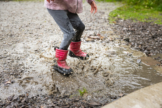 Low section of girl wearing boots and jumping in water puddle