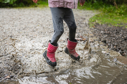 Low section of girl jumping in muddy water puddle