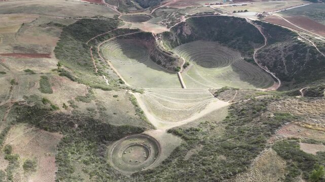Smooth aerial flight over Moray Incan agricultural terraces in the Sacred Valley, Peru, captured in crisp daylight with light cloud cover.