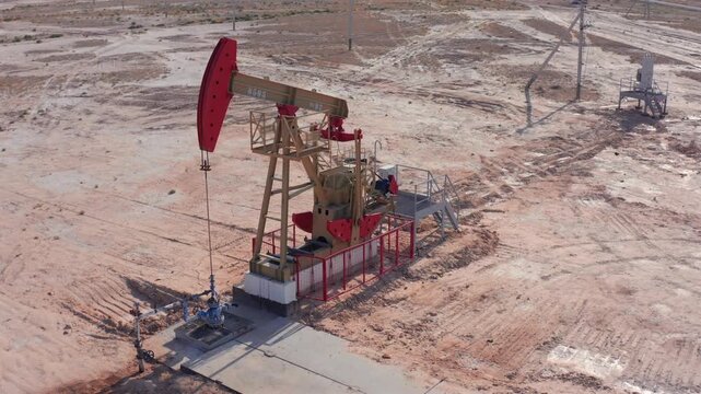 Single oil pumpjack with red details working in isolated desert oilfield. Drone view sandy landscape, dry soil, sparse vegetation, and sense of industrial isolation in energy extraction site.