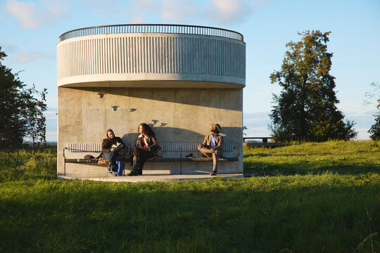 Male and female visitors spending leisure time sitting on bench at shelter in park