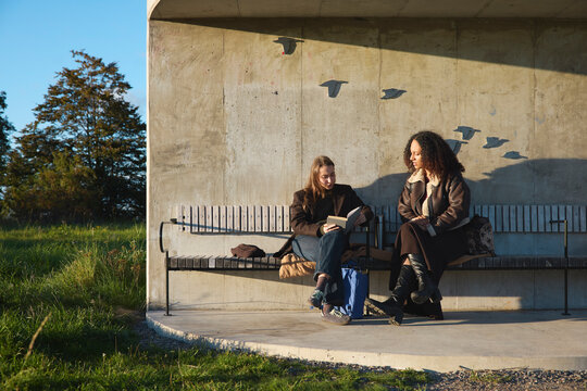 Woman reading book while sitting next to female friend on bench at park