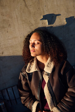 Woman sitting with eyes closed in sunlight at park