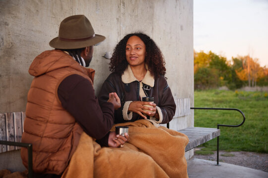Smiling woman holding coffee cup and listening to man talking while sitting on bench