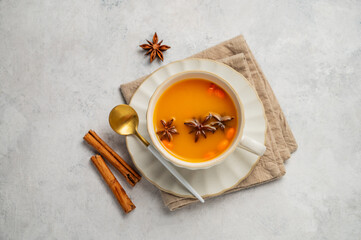 Sea buckthorn herbal tea in a cup on a light background with spices, spoon and napkin.