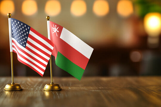 United States USA and Oman small desk flags on wooden table - diplomatic relations concept with copy space - Powered by Adobe