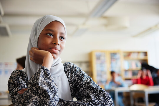 Schoolgirl in hijab sitting leaning on elbow while sitting in classroom