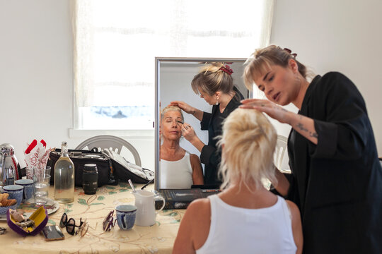 Reflection of female beautician doing eye make-up of fashion model with brush seen in mirror at studio