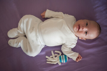 Adorable baby is lying on a purple blanket in white clothes. Next to the infant is a blue and white octopus toy. The baby is looking directly at the camera