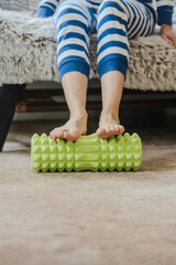 Closeup photo of young woman massaging legs with fitness foam roller. Foot massage at home using a textured roller for muscle relaxation