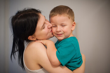 A young woman, the older sister, is holding and kissing her little brother on the cheek. The boy is smiling and looks happy. It's a sweet, tender moment between siblings