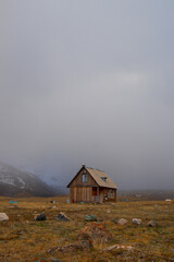 Isolated wooden cabin in a remote mountain valley surrounded by heavy mist and grey overcast sky
