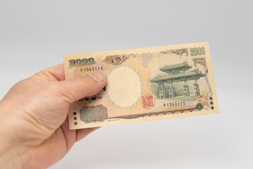 Hand holding a rare Japanese 2000 Yen banknote featuring the Shureimon Gate on a white background. Japan economy and finance concept.