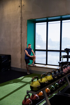Man standing with leg on window sill while taking break after exercising in gym