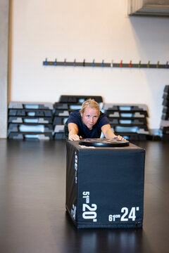 Dedicated woman pushing heavy box while doing strength training in gym