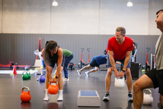 Young woman lifting kettlebell while training with friend in gym