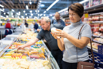Elderly woman choose cheese in supermarket