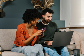 Young cheerful couple shopping at home with credit card and laptop, buying on online retail shop 