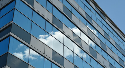 Fototapeta premium Modern glass building facade with clear blue sky and fluffy white clouds reflected in symmetrical window panels