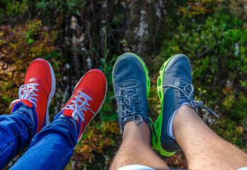 Two pairs of legs wearing vibrant red and gray-green sneakers dangle over a dark, mossy forest floor, symbolizing outdoor adventure and leisure.