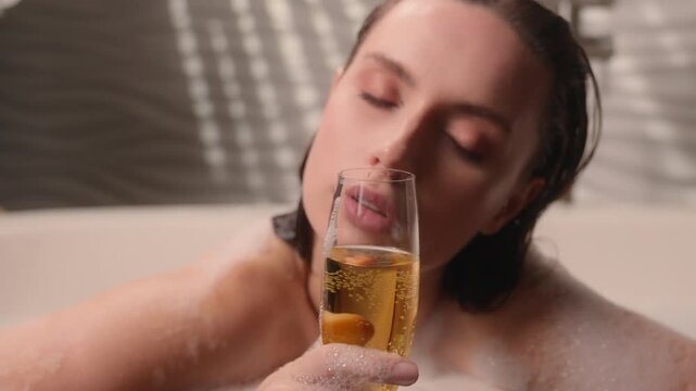 Close up Caucasian drunk woman drinking wine glass champagne at bath hotel bathing beautiful female sensual girl lady enjoying holding drink foamy alcohol spa relaxing soapy bathtub recreation relief
