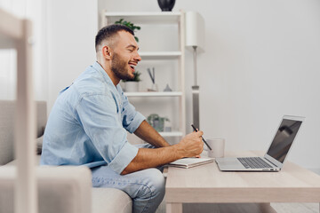 Young man enjoying remote work at home, smiling while using laptop, reflecting on work-life balance and embracing a mindful approach to productivity.
