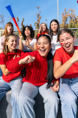 Fototapeta premium Multiethnic women friends cheering enthusiastically, supporting their team at a vibrant stadium sport event