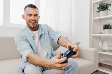 Happy man enjoying video games in a modern living room, dressed casually in denim, showcasing a joyful lifestyle that blends leisure and technology.