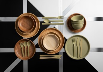 A stylish arrangement of wooden plates and green ceramic bowls with matching flatware on a geometric black and white surface, showcasing modern and natural dining aesthetics.