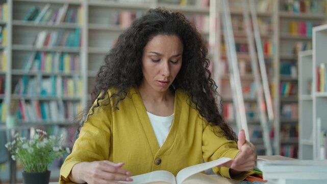 Confused shocked Latina Arabian woman reading book in library female girl student studying exam preparation puzzled amazed difficulty search information university high school education learning focus