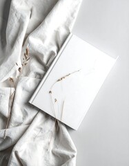 White book with delicate dried grass on a linen cloth, creating a minimalist and serene composition.