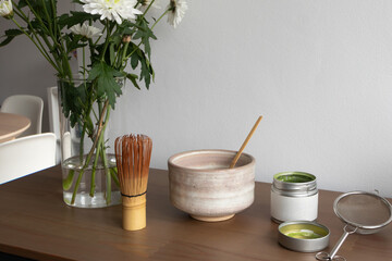 Matcha preparation setup with ceramic bowl bamboo whisk, open tin of matcha powder, mesh strainer on wooden table