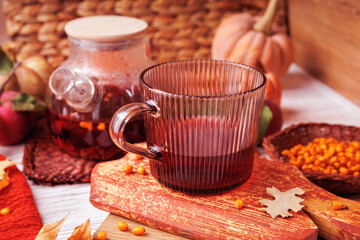 Glass mug of herbal red tea on rustic wood with teapot, pumpkins, apple and basket of sea buckthorn berries