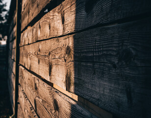 Weathered wooden planks bathed in dramatic sunlight and deep shadows, revealing rich, rustic texture.