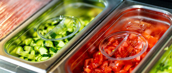Metal containers filled with various sliced vegetables and ingredients in a professional kitchen setting
