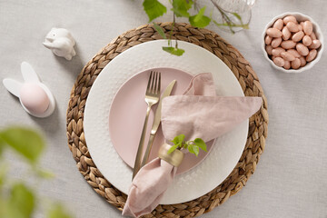 Soft Easter table setting with pink plate, linen napkin, gold cutlery and spring accents. Elegant pastel holiday composition.