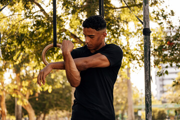 Athlete stretching shoulder before a calisthenics workout on gym rings in an outdoor park. Warmup, focus, mobility, and healthy training routine