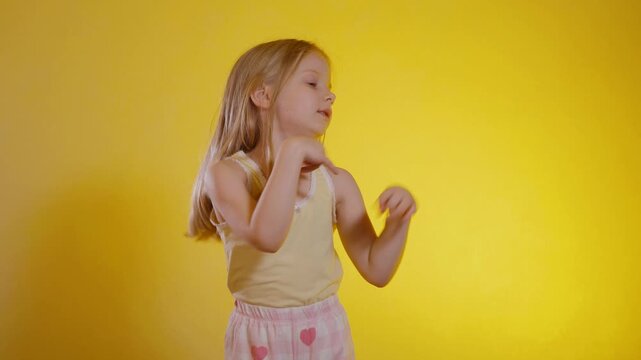 Joyful young girl with long blonde hair celebrating or dancing against a vibrant, sunny yellow backdrop, wearing a light yellow tank top and patterned shorts. Child raising both fists enthusiastically