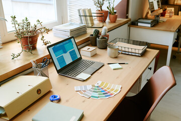Modern workspace featuring open laptop displaying business presentation, color swatches, sticky notes, coffee mug, potted plants, office supplies arranged on wooden desk