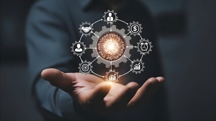 Close-up of a person's hand holding a glowing gear icon with various social and business symbols floating above it in a dark room with cinematic lighting.