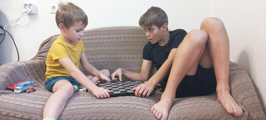 Two boys are playing chess on a sofa in their home. © ANASTASIIA