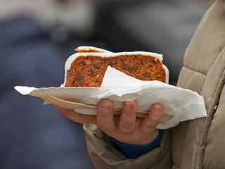 A generous slice of homemade carrot cake with a citrus sugar glaze served at Prague lively Naplavka farmers market, where big portions and comforting flavors attract weekend visitors.