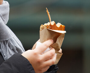 Visitor holding warm street-food snack at winter Naplavka farmers market in Prague during advent season, showcasing seasonal outdoor eating and market atmosphere.