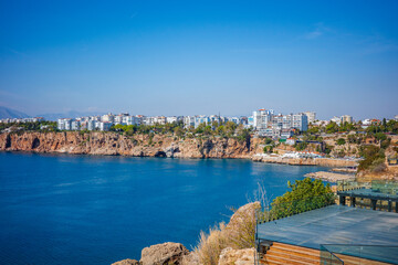 A bright panoramic view of Antalya’s rugged coastal cliffs bordering the deep blue Mediterranean Sea, with modern residential buildings lining the shoreline